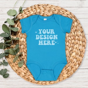 Könnte beinhalten: Ein türkisfarbener Baby-Strampler mit kurzen Ärmeln und Druckknöpfen. Der Strampler hat den Text "YOUR DESIGN HERE" in weißer Retro-Schrift auf der Vorderseite.