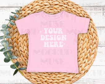 May include: Pink baby t-shirt with a woven straw mat background. The t-shirt has the text "YOUR DESIGN HERE" in white.