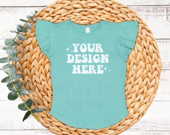 May include: A turquoise blue t-shirt with short, ruffled sleeves. The shirt has a white graphic that says "YOUR DESIGN HERE" with stars on either side of the text.