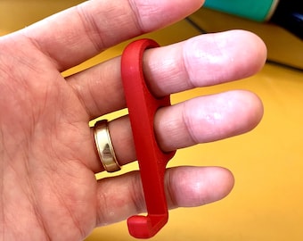 Puede incluir: Un ejercitador de dedos de plástico rojo con dos bucles para los dedos. El ejercitador está diseñado para ayudar a fortalecer y mejorar la destreza de los dedos.