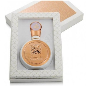 May include: A white and gold round bottle of perfume with a gold cap and a gold label that says "The Secret of Oud" in Arabic. The bottle is in a white box with a gold pattern.
