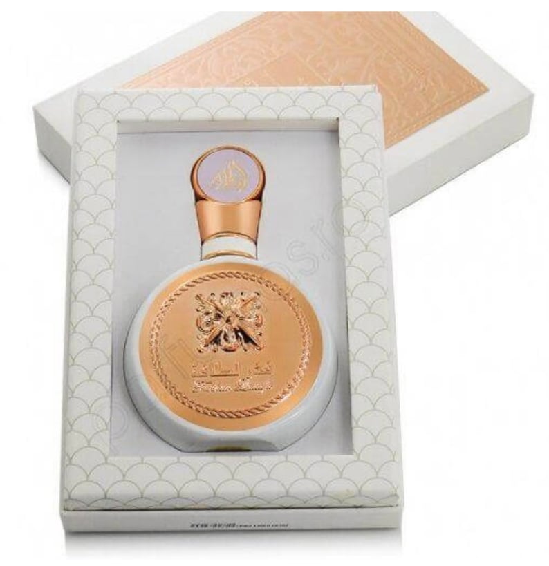 May include: A white and gold round bottle of perfume with a gold cap and a gold label that says "The Secret of Oud" in Arabic. The bottle is in a white box with a gold pattern.