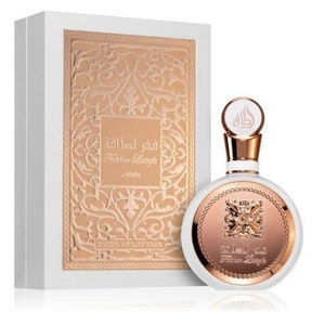 May include: A white bottle of perfume with a gold cap and a gold label. The label has Arabic text and the words "Fakhar Lattafa" and "Lattafa" in English. The bottle is sitting on a white box with a gold design.
