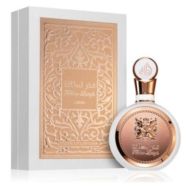 May include: A white bottle of perfume with a gold cap and a gold label. The label has Arabic text and the words "Fakhar Lattafa" and "Lattafa" in English. The bottle is sitting on a white box with a gold design.
