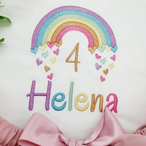 Puede incluir: Una camiseta blanca con un arco&iacute;ris bordado, corazones peque&ntilde;os, el n&uacute;mero 4 y el nombre Helena en hilo multicolor. Debajo, una falda de tul rosa empolvado con un lazo de cinta de sat&eacute;n a juego en el centro de la cintura.