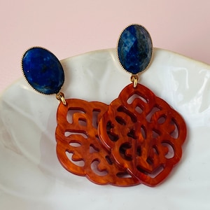 Könnte beinhalten: Ein Paar Ohrringe mit blauen Edelstein-Cabochons und aufwendig geschnitzten Holzdetails. Die Ohrringe sind in einem satten Braun gehalten und haben ein zartes, verziertes Design.