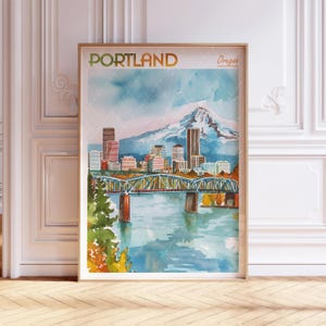 May include: A framed watercolor print of Portland, Oregon, featuring a bridge, cityscape, and a snow-capped mountain. The word "PORTLAND" is at the top, with "Oregon" below it. The artwork is in a wooden frame.
