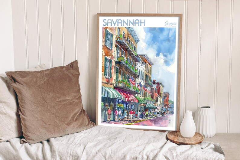 May include: A watercolor painting of a street scene in Savannah, Georgia. The painting depicts a row of colorful buildings with balconies and awnings. There are people walking on the street and trees lining the sidewalk. The painting is framed in a wooden frame.