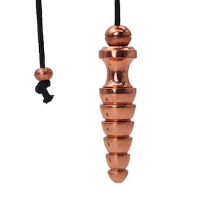 May include: A copper pendulum with a black cord and a small copper bead. The pendulum has a cylindrical shape with a series of stacked, rounded segments. The top of the pendulum has a spherical bead.