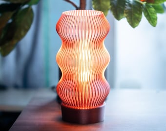 May include: A pink and orange table lamp with a wavy, ribbed glass shade. The lamp is turned on and the light is shining through the glass.