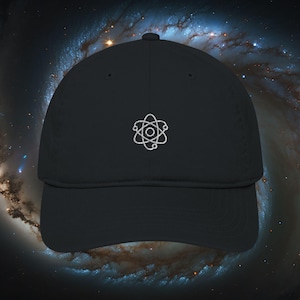 May include: Black baseball cap with a curved brim. The cap features a white embroidered atom symbol on the front. The background shows a galaxy.