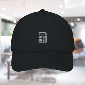 May include: Black baseball cap with a white embroidered calculator design on the front. The cap has a curved brim and a structured fit. The design is simple and clean, making it a versatile accessory.