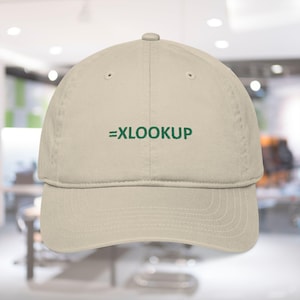 May include: A beige baseball cap with the text "=XLOOKUP" embroidered in green across the front. The cap has a curved brim and a classic six-panel design. The background is blurred.