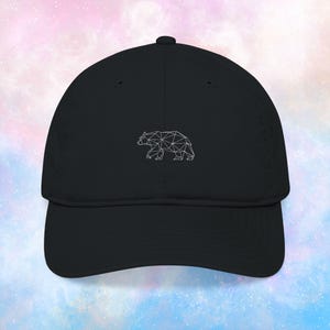 May include: Black baseball cap featuring a geometric bear design in white. The cap has a curved brim and an adjustable strap at the back. This hat is a stylish accessory for outdoor activities or casual wear.