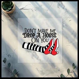 May include: A square print with the text "Don't Make Me Drop A House On You." The image features a pair of red shoes and striped black and white stockings, reminiscent of the Wicked Witch of the East from The Wizard of Oz.