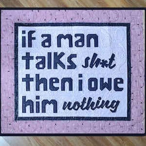 Könnte beinhalten: Eine gesteppte Wandbehänge mit dem Text "if a man talks sh*t then i owe him nothing" in dunkelblauen Buchstaben. Der Hintergrund ist weiß mit einem rosa Rand mit Mond- und Sternmustern.