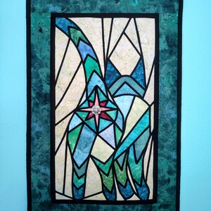 May include: A teal blue and green stained glass style wall hanging featuring a cat with a large pink and blue star in the center.