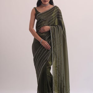 以下が含まれることがあります： 銀色の刺繍が施された濃い緑色のサリー。サリーは繊細で複雑なデザインで、上品な光沢があります。生地は柔らかく、しなやかで、特別な機会に最適です。