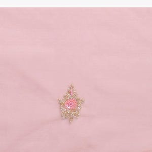 May include: A light pink fabric labeled Saree Body featuring a central floral motif and a bottom border. The embroidery consists of small pink and peach sequins, beads, and metallic gold thread forming delicate flower and leaf patterns.