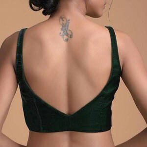 Pode incluir: Uma blusa sem mangas de veludo verde-escuro com um decote profundo em V nas costas e al&ccedil;as largas. A pe&ccedil;a &eacute; constru&iacute;da com costuras verticais ao longo dos pain&eacute;is traseiros, proporcionando um ajuste estruturado com um acabamento macio.