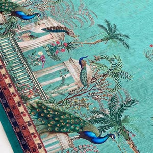 May include: A teal fabric featuring a repeating pattern of peacocks, classical architectural structures with columns, and palm trees. The design includes small pink floral accents and a decorative border with geometric patterns in red and blue.