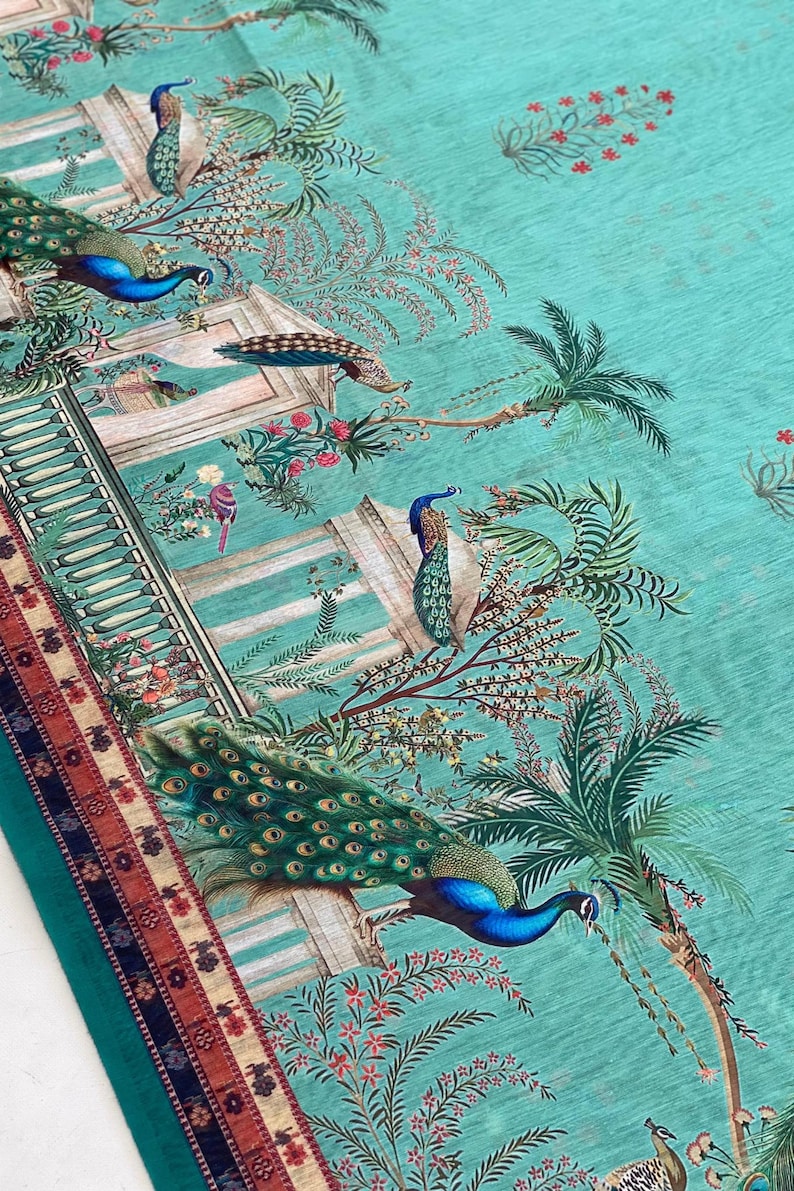 May include: A teal fabric featuring a repeating pattern of peacocks, classical architectural structures with columns, and palm trees. The design includes small pink floral accents and a decorative border with geometric patterns in red and blue.