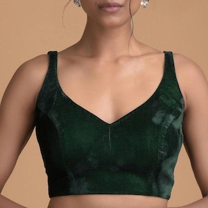 Pode incluir: Uma blusa sem mangas em veludo verde esmeralda escuro com um decote em V profundo e al&ccedil;as largas. A pe&ccedil;a &eacute; constru&iacute;da com detalhes de costura vertical na parte frontal, criando um ajuste estruturado com uma textura suave e reflexiva.