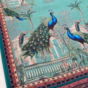 May include: A teal fabric featuring a repeating print of peacocks with vibrant blue and green plumage, palm trees, and classical architectural structures. The bottom edge is finished with a decorative border in shades of red, orange, and black.
