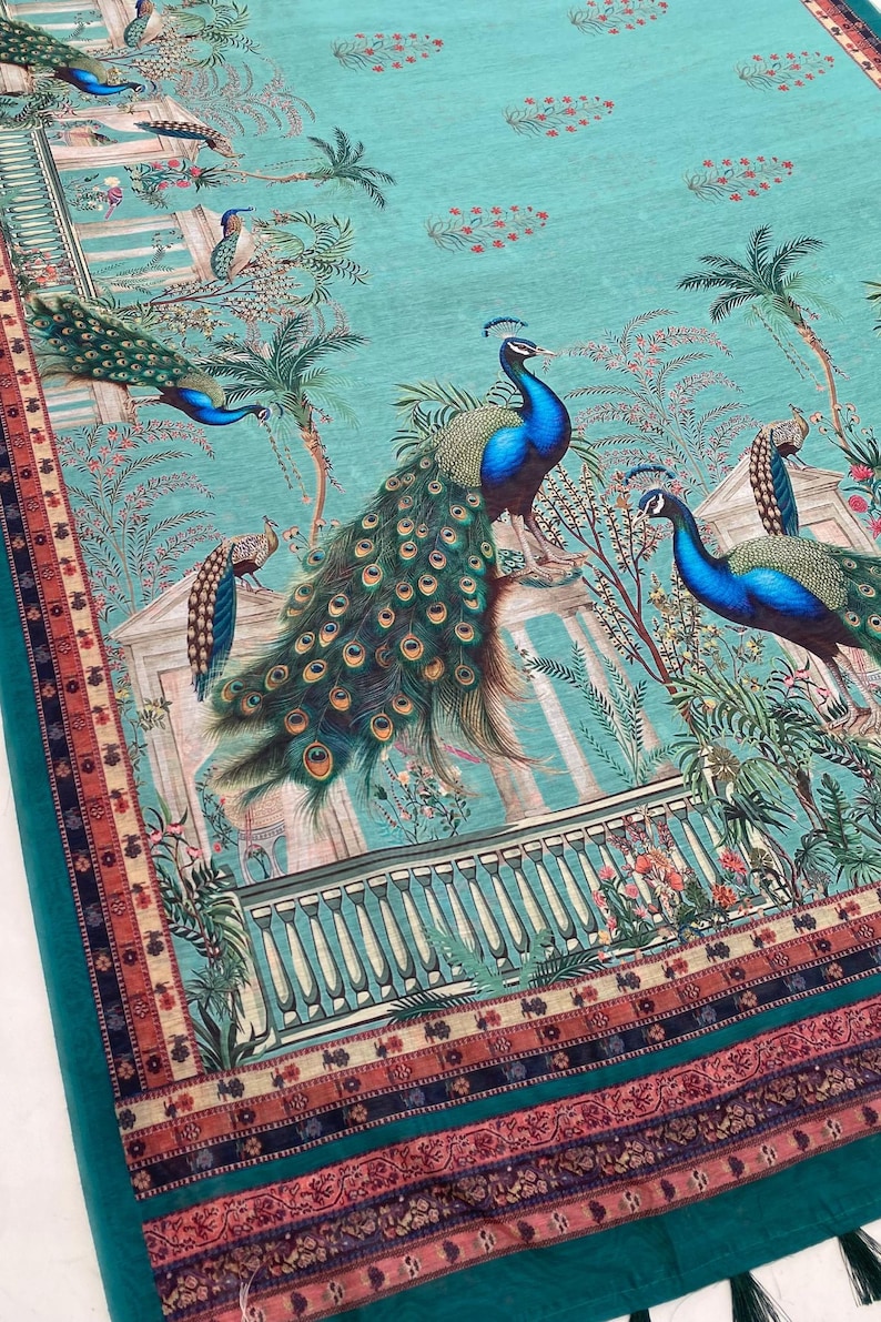 May include: A teal fabric featuring a repeating print of peacocks with vibrant blue and green plumage, palm trees, and classical architectural structures. The bottom edge is finished with a decorative border in shades of red, orange, and black.