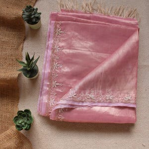 Pu&ograve; includere: Una sciarpa rosa polvere piegata con una lucentezza sottile e un bordo delicatamente ricamato con motivi floreali in filo d'argento. La sciarpa &egrave; rifinita con frange beige chiaro sul bordo superiore, realizzata in un tessuto morbido e leggero.