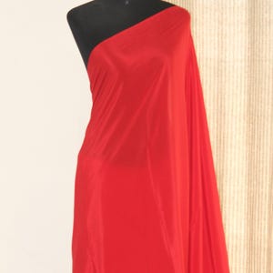 Könnte beinhalten: Ein leuchtend roter Stoff, der über einer schwarzen Schaufensterpuppe drapiert ist. Der Stoff ist glatt und scheint ein leichtes Material zu sein, möglicherweise Seide oder Satin. Der Stoff ist drapiert, um einen One-Shoulder-Effekt zu erzeugen.