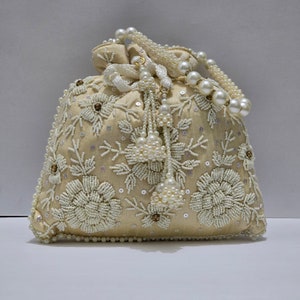 May include: A cream-colored drawstring bag with a pearl and beaded floral design. The bag has a long pearl and beaded strap.