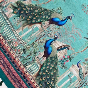 May include: A teal fabric featuring a repeating pattern of peacocks with iridescent blue and green plumage. The design includes architectural structures, palm trees, and floral elements. The edge has a decorative border with tassels.
