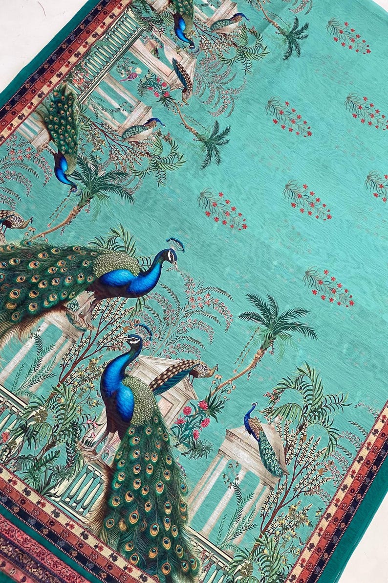May include: A teal fabric featuring a repeating pattern of peacocks with iridescent blue and green plumage, palm trees, and classical architectural columns. Small red floral motifs are scattered across the background, framed by a decorative border.