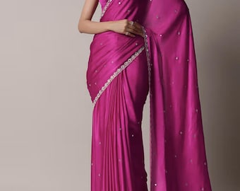May include: A vibrant magenta saree featuring a smooth, satin-like finish with scattered small circular mirror embellishments throughout the fabric. The garment includes a matching sleeveless blouse and a decorative border with intricate silver embroidery.