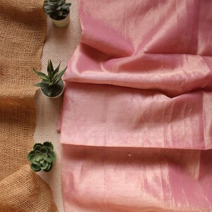 Pu&ograve; includere: Un tessuto rosa chiaro con una lucentezza sottile e una consistenza semi-trasparente. Il tessuto presenta un ricamo delicato e complesso lungo i bordi superiore e inferiore, composto da piccoli motivi floreali accentuati da minuscole perline argentate.