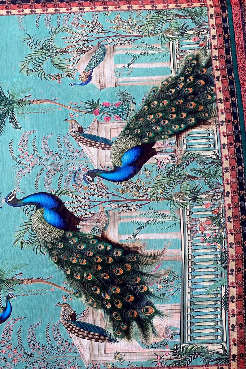 May include: A fabric textile featuring a repeating pattern of vibrant blue and green peacocks with long, detailed tail feathers. The scene includes architectural stone columns, lush palm trees, and floral elements set against a bright turquoise background.