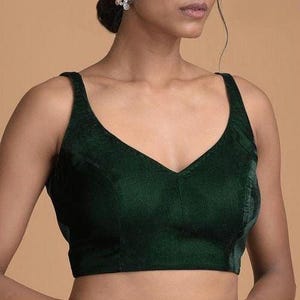 Pode incluir: Uma blusa sem mangas de veludo verde-escuro com um decote em V profundo e al&ccedil;as largas. A pe&ccedil;a &eacute; constru&iacute;da com detalhes de costura vertical ao longo da parte frontal do corpete, proporcionando um ajuste estruturado at&eacute; a cintura.