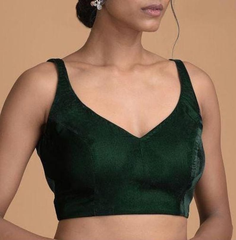 Pode incluir: Uma blusa sem mangas de veludo verde-escuro com um decote em V profundo e al&ccedil;as largas. A pe&ccedil;a &eacute; constru&iacute;da com detalhes de costura vertical ao longo da parte frontal do corpete, proporcionando um ajuste estruturado at&eacute; a cintura.