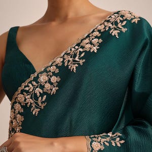 May include: A deep emerald green sleeveless blouse featuring a V-neckline and a textured fabric. The garment is adorned with intricate light gold floral embroidery and sequin detailing along the neckline and the sleeve edge.
