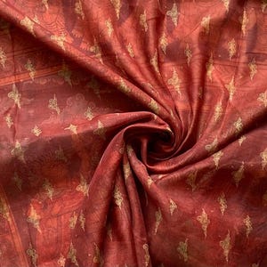 May include: A deep red fabric featuring a repeating gold-colored pattern of small, stylized floral or leaf-like motifs. The material has a translucent, lightweight quality with visible folds and gathers that create a swirling, textured appearance.