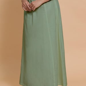 May include: A sage green skirt with a drawstring waist. The skirt is long and flowing, made of a lightweight fabric. The person is wearing brown embroidered flats.
