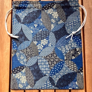 May include: A rectangular fabric drawstring pouch featuring a repeating pattern of interlocking circles in various shades of blue, navy, and white. The design incorporates diverse floral and geometric motifs within each circular segment, finished with white cord.