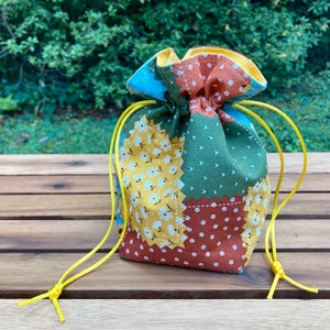 Peut inclure: Un petit sac &agrave; cordon en tissu patchwork avec un motif floral jaune, vert, marron et bleu. Le sac a un cordon jaune.