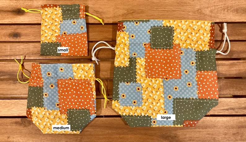 Peut inclure: Trois sacs &agrave; cordon en tissu patchwork de diff&eacute;rentes tailles&nbsp;: petit, moyen et grand. Les sacs sont faits de diff&eacute;rents tissus dans des tons de bleu, vert, jaune et orange. Les sacs sont tous attach&eacute;s avec des cordons de serrage blancs.