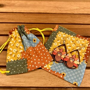 Peut inclure: Une paire de boucles d'oreilles en bois en forme de dinde avec un motif peint brun, orange et jaune. Les boucles d'oreilles sont dans un petit sac en tissu patchwork avec des cordons jaunes.