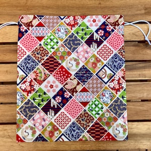 Könnte beinhalten: Eine Kordeltasche mit Patchwork-Muster in verschiedenen Farben und Mustern, darunter Rot, Blau, Grün und Weiß. Die Tasche ist aus Stoff und hat eine weiße Kordel.