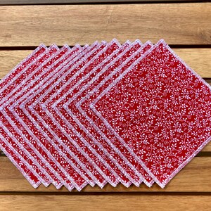 以下が含まれることがあります： 赤と白の模様の布ナプキンの束。各正方形のナプキンは、赤い背景に白い繰り返し模様のフローラルデザインが特徴です。エッジは白い装飾的なステッチで仕上げられています。