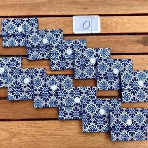 May include: A collection of small, patterned fabric wallets with a blue and white floral design. Each wallet has a white button closure. The wallets are arranged on a wooden surface, with a small white tag labeled "0".