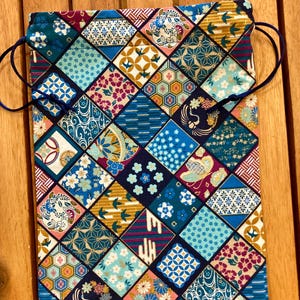 Może przedstawiać: Worek ze sznurkiem ze wzorem patchwork. Torba posiada różnorodne geometryczne i kwiatowe wzory w odcieniach niebieskiego, turkusowego, złotego, różowego i fioletowego. Sznurek to ciemnoniebieski sznurek.
